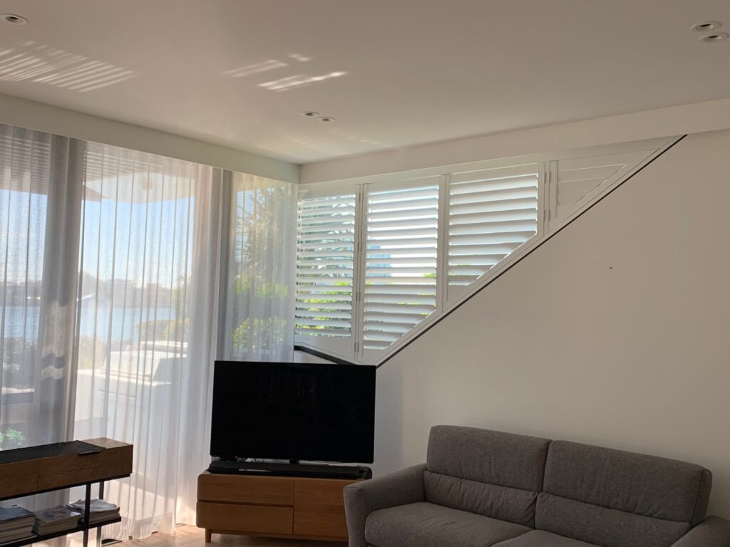 Custom shaped white PVC plantation shutter fitted to a raked living room window in Bulimba