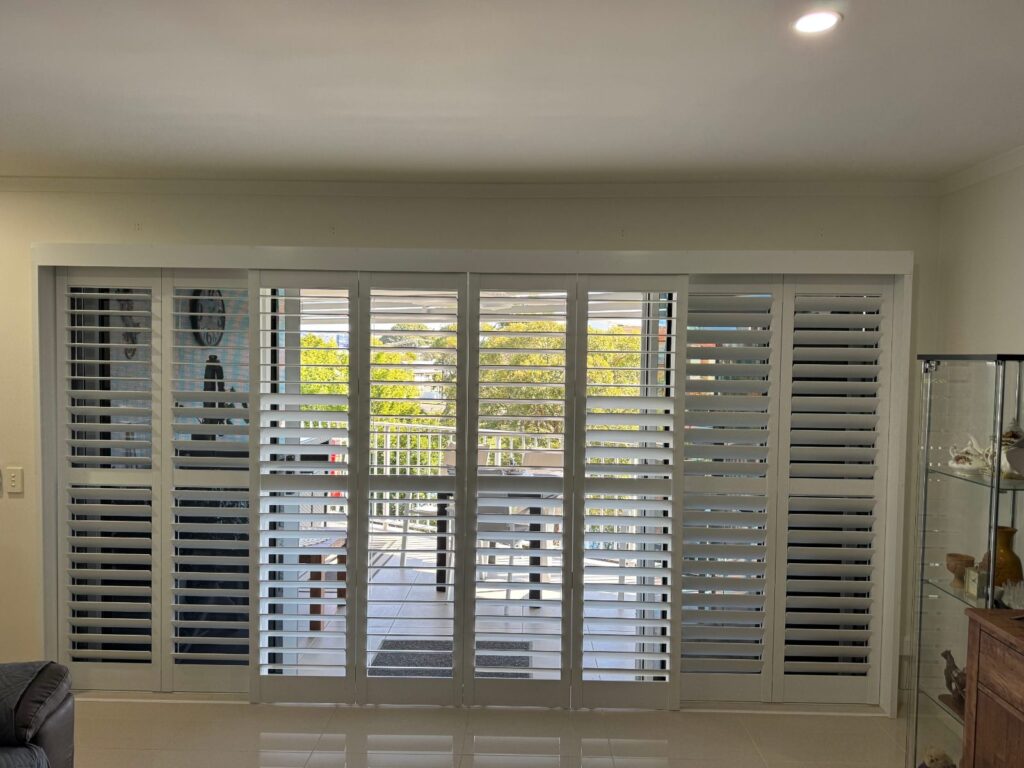 White PVC plantation shutters installed across a living room window in Redcliffe