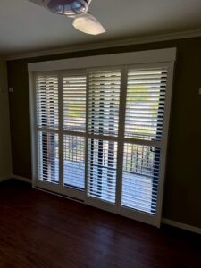 Four white PVC plantation shutter panels fitted across a full-height door opening in a Caboolture home, louvres tilted open above the mid rail